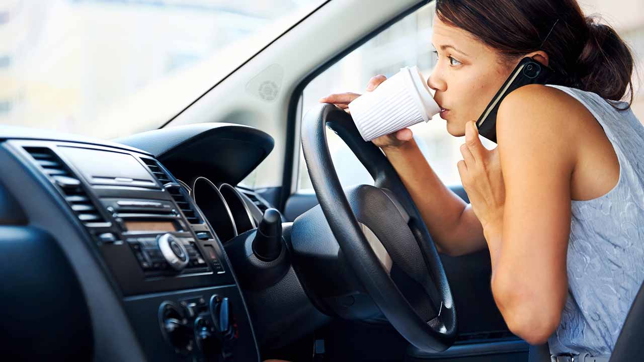 person driving, drinking coffee, and trying to talk on phone all at the same time.