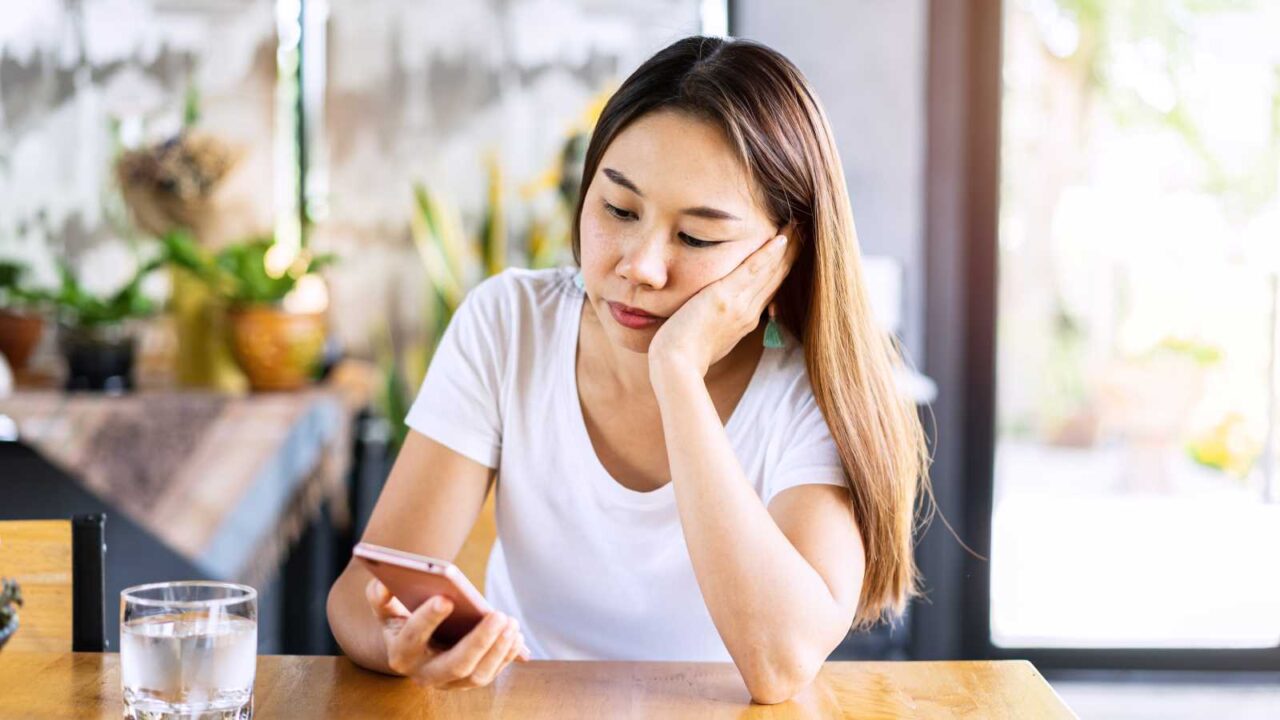 Bored woman looking disappointed at her smart phone while waiting for someone in restaurant.